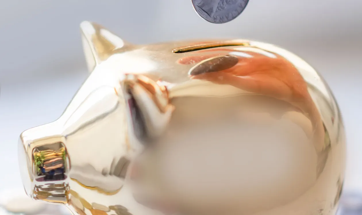 Hand placing a coin into a golden piggy bank near financial paperwork