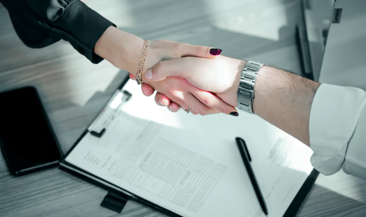 Employer and new employee shaking hands over a signed contract